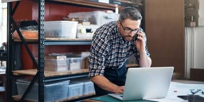 Man bellend staand bij laptop in magazijn